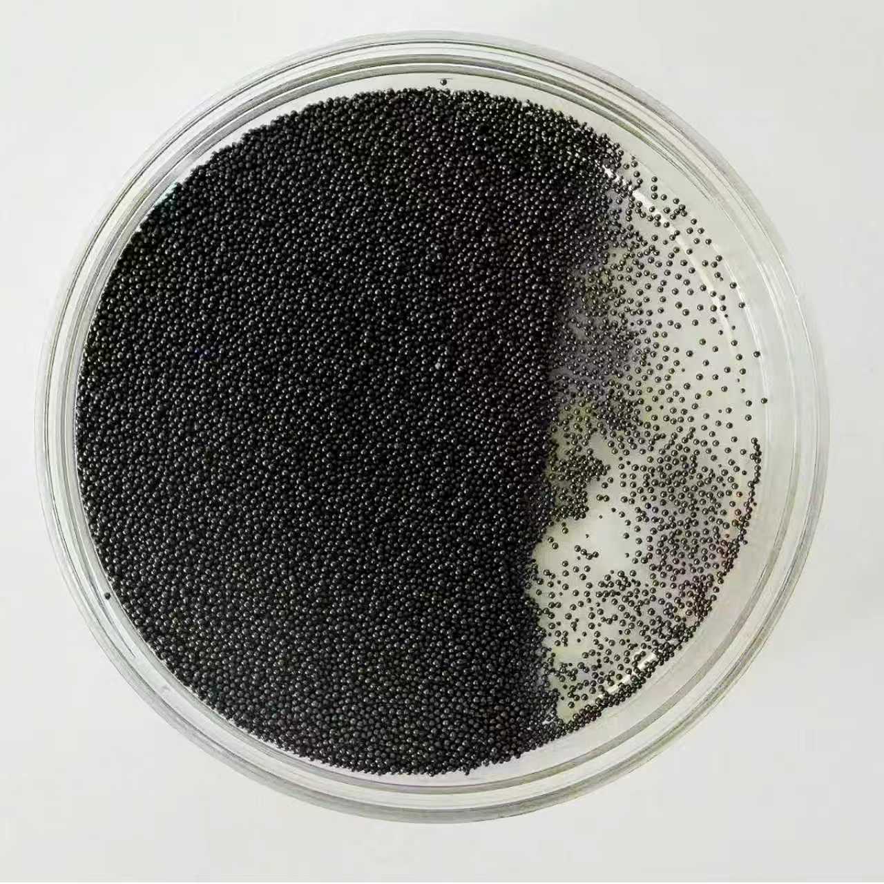 Spherical activated carbon beads, black, in a glass dish on white background